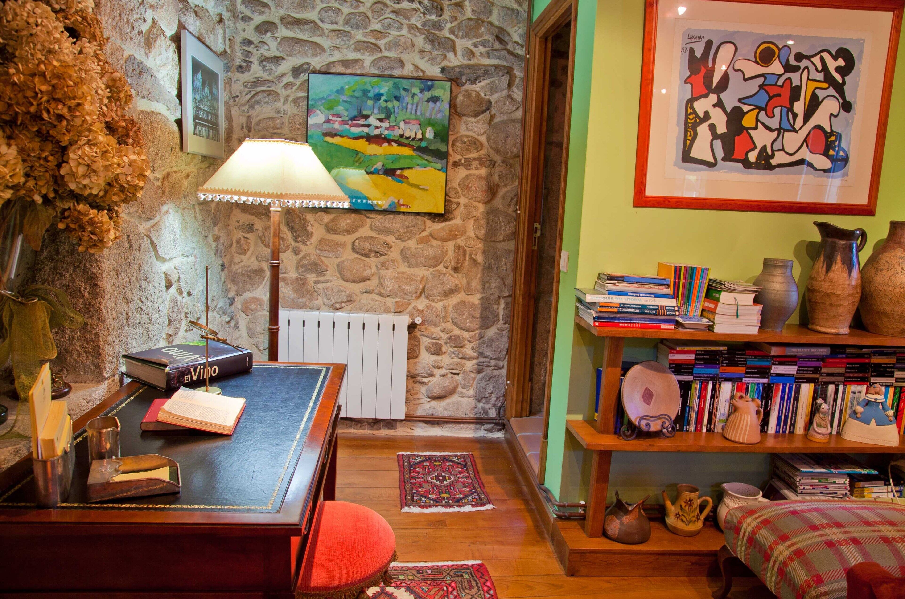 Una camera accogliente con una parete in pietra, una scrivania in legno con libri, una lampada e una libreria piena di libri e oggetti decorativi.