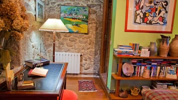 Una habitación acogedora con una pared de piedra, un escritorio de madera con libros, una lámpara y una estantería llena de libros y objetos decorativos.