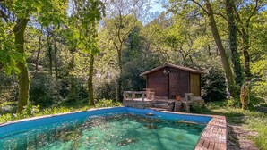 Una piscina nítida amb un tramuntana de fusta, envoltada de vegetació exuberant i una petita cabana de fusta.