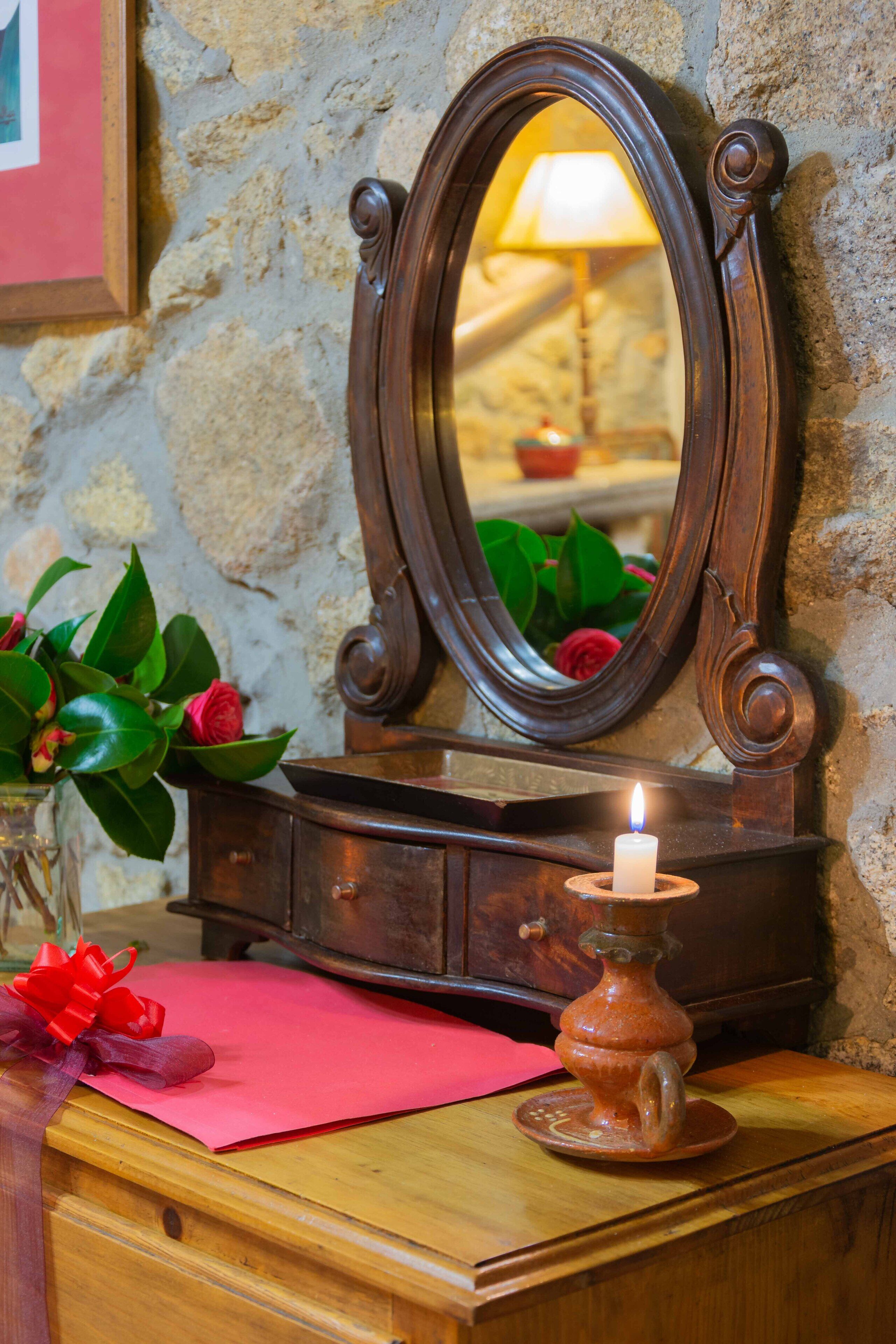 Un aparador de madera con un espejo, una vela encendida y un florero con hojas verdes y una rosa roja.