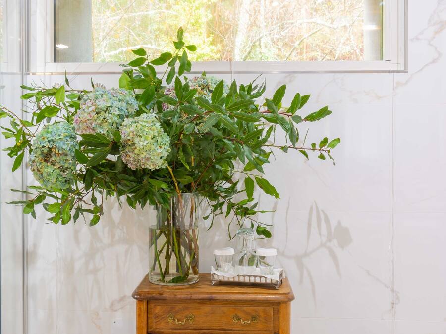 Una mesa de madera con un florero y un estante con botellas.