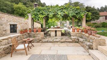 A stone patio with a table and chairs, surrounded by potted plants and a pergola with vines.