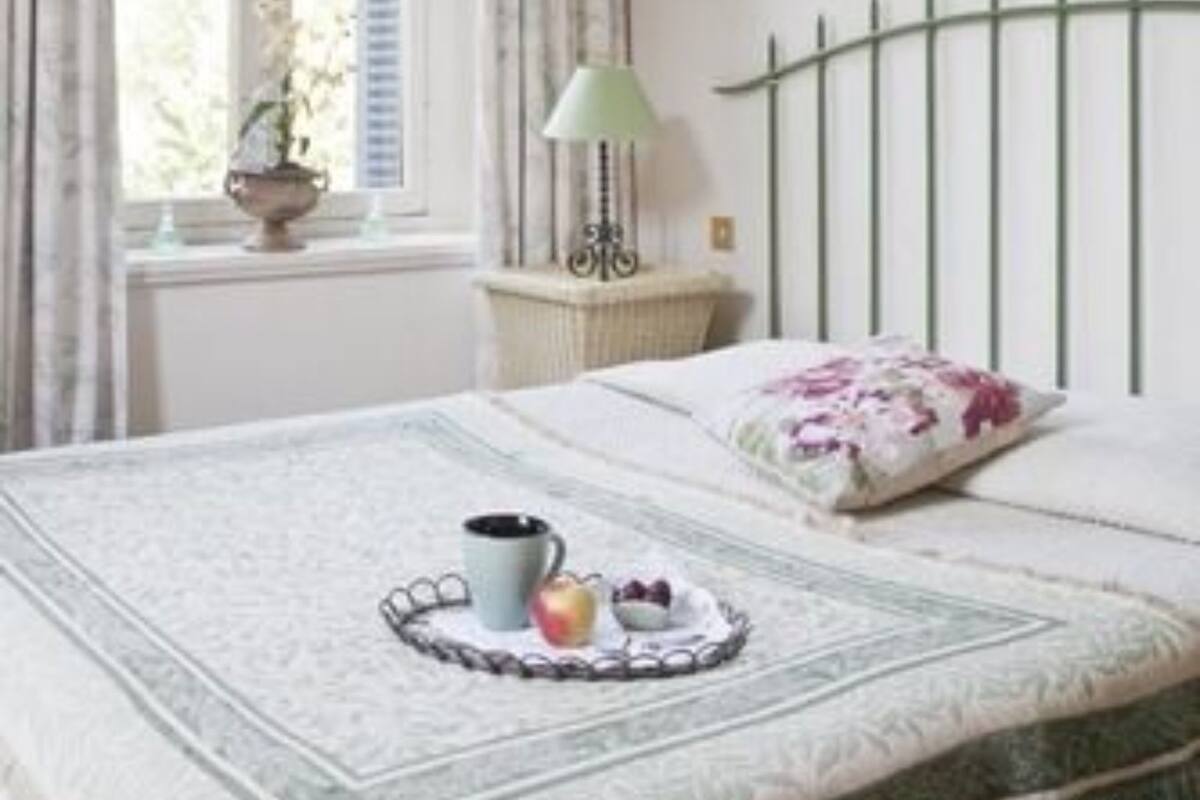A bedroom with a bed, a window with curtains, a lamp, a wall painting, and a bedside table with a tray of fruit.