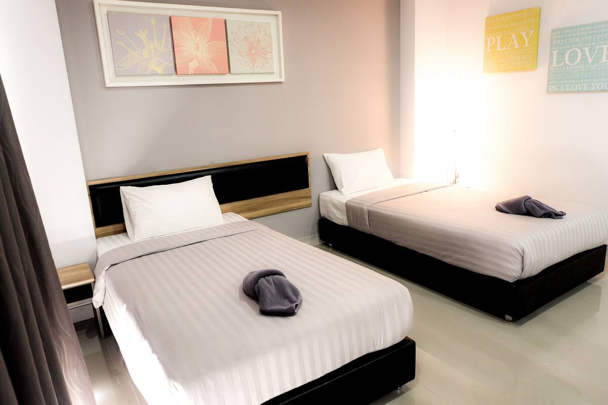 A hotel room with two beds, each with a wooden headboard and white bedding. There are framed artworks on the wall and motivational posters.