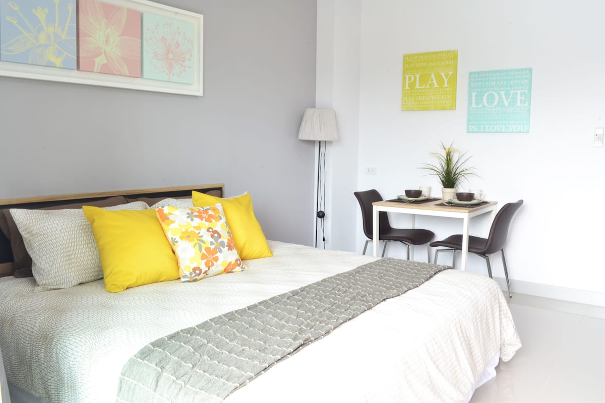 A neatly arranged bedroom with a bed, bedside table, chairs, and a desk.