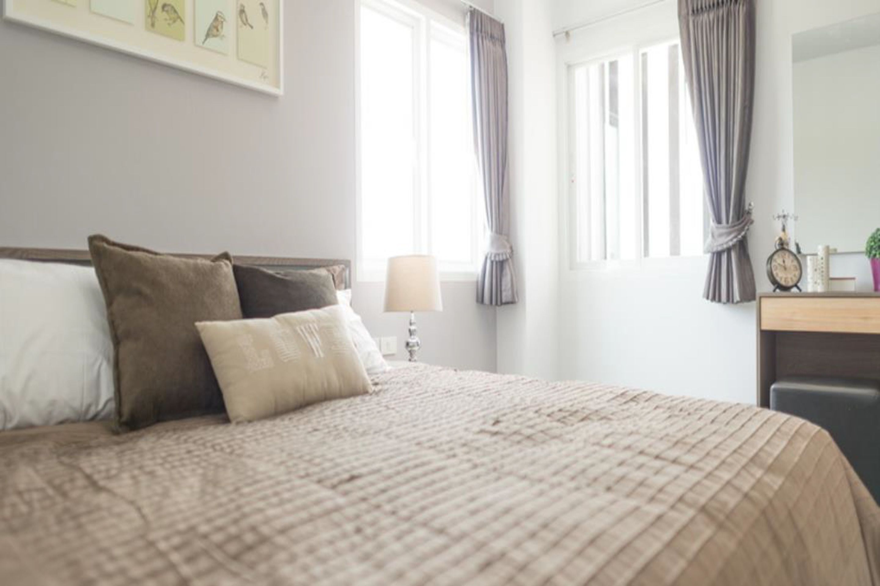 A neatly made bed with a beige quilt, a bedside lamp, and a framed picture on the wall.