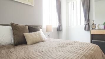 A neatly made bed with a beige quilt, a bedside lamp, and a framed picture on the wall.