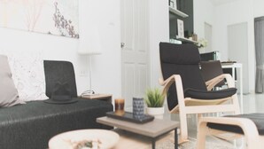 Ein modernes Wohnzimmer mit einer Couch, einem schwarzen Sessel, einem kleinen Tisch mit Teller und einem Blumentopf.