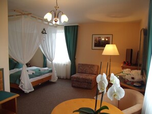 Habitación de hotel con cama, una silla, una mesa con flores, una lámpara y un cuadro en la pared.