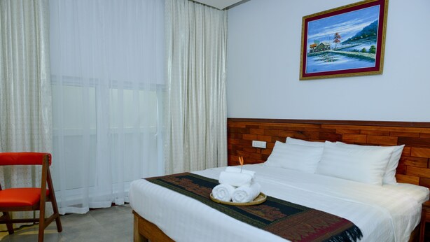 Una habitación de hotel con una cama grande, cabecera de madera, ropa de cama blanca, una silla roja y un cuadro en la pared.