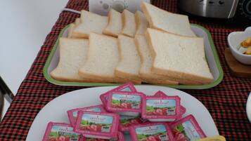 A table with a checkered tablecloth, a toaster, a blender, and plates of sliced bread and cheese packets.