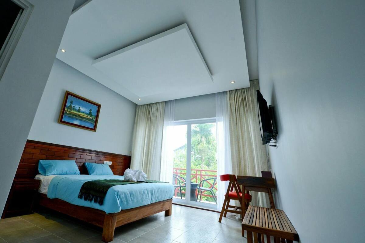 A bedroom with a bed, a TV mounted on the wall, and a balcony with chairs.