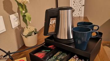 Eine Kaffeemaschine, zwei blaue Tassen, ein Blumentopf, eine Schublade mit Kaffeepads und ein Rauchverbotsschild auf einem Holztisch.