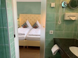 Un dormitorio con dos camas, una mesita de noche y un baño con lavabo y espejo.