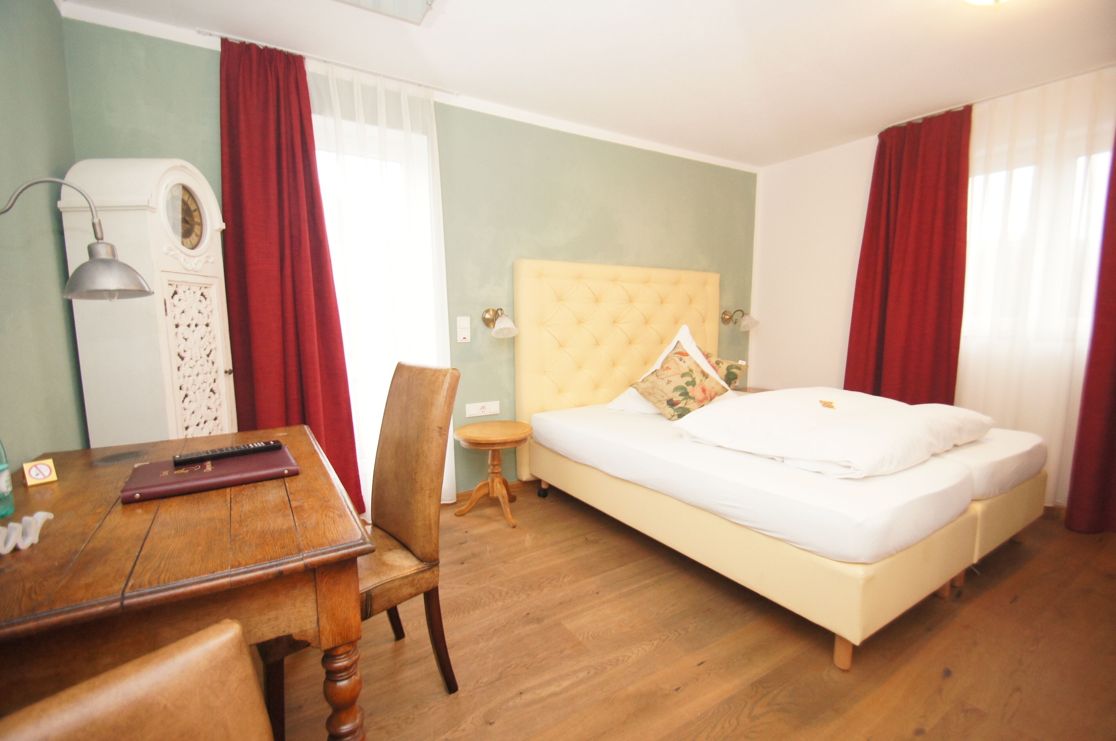 A bedroom with a bed, a desk, a chair, a small table, and a lamp.