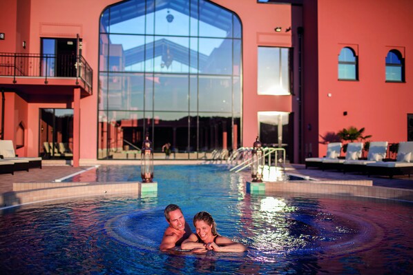 A couple in a swimming pool with a large glass building in the background.