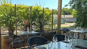 Un patio al aire libre con mesas y sillas, rodeado de follaje y una terraza de madera.