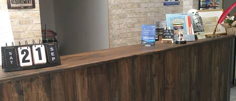 A reception desk with a rustic wooden finish, a framed sign above it, and a wall clock displaying 21.