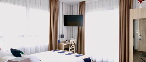A hotel room with a bed, a desk, a chair, a TV, and a door.