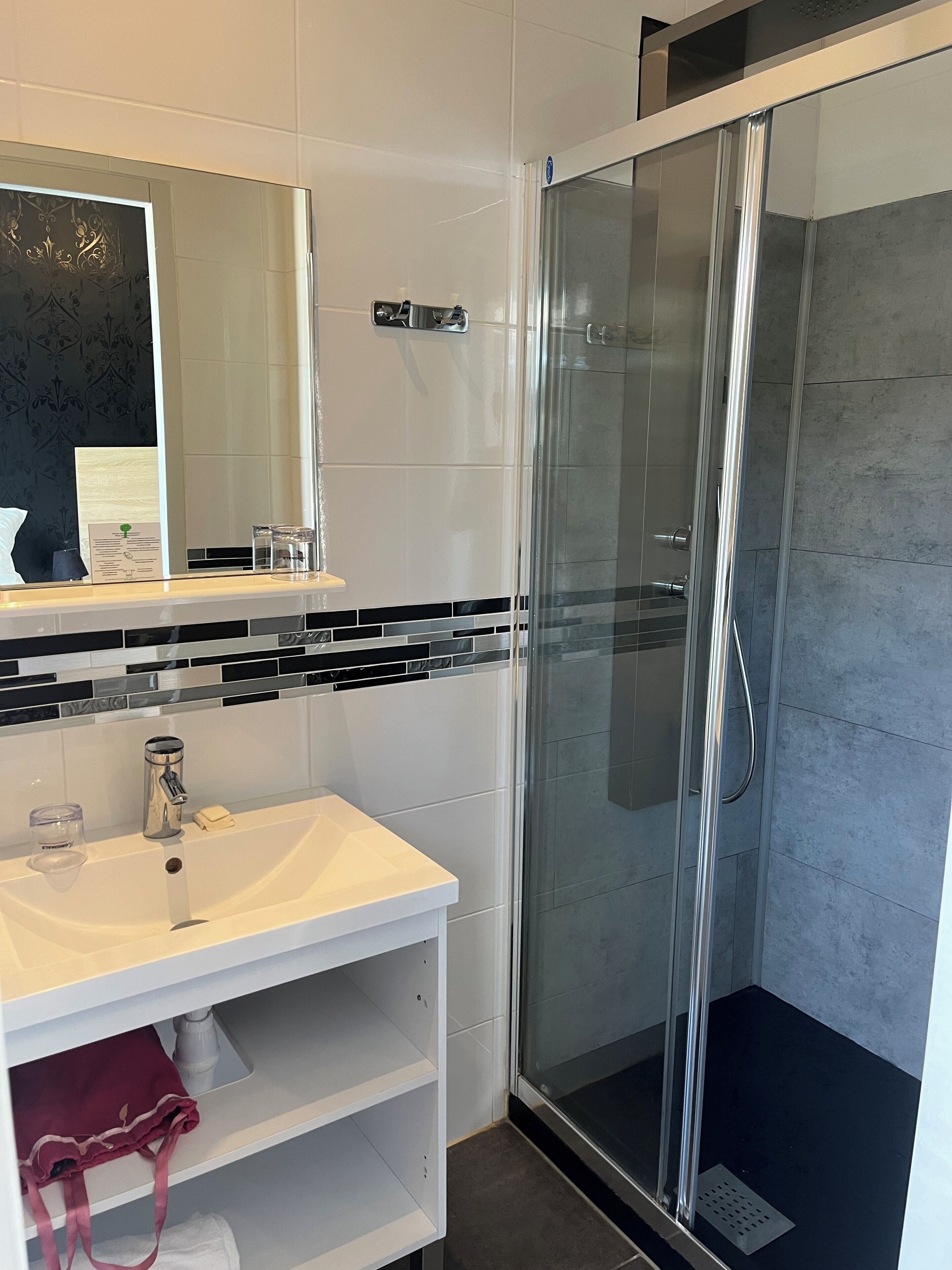 Une salle de bain moderne avec un lavabo blanc, une cabine de douche en verre et un miroir doté d’un cadre décoratif.
