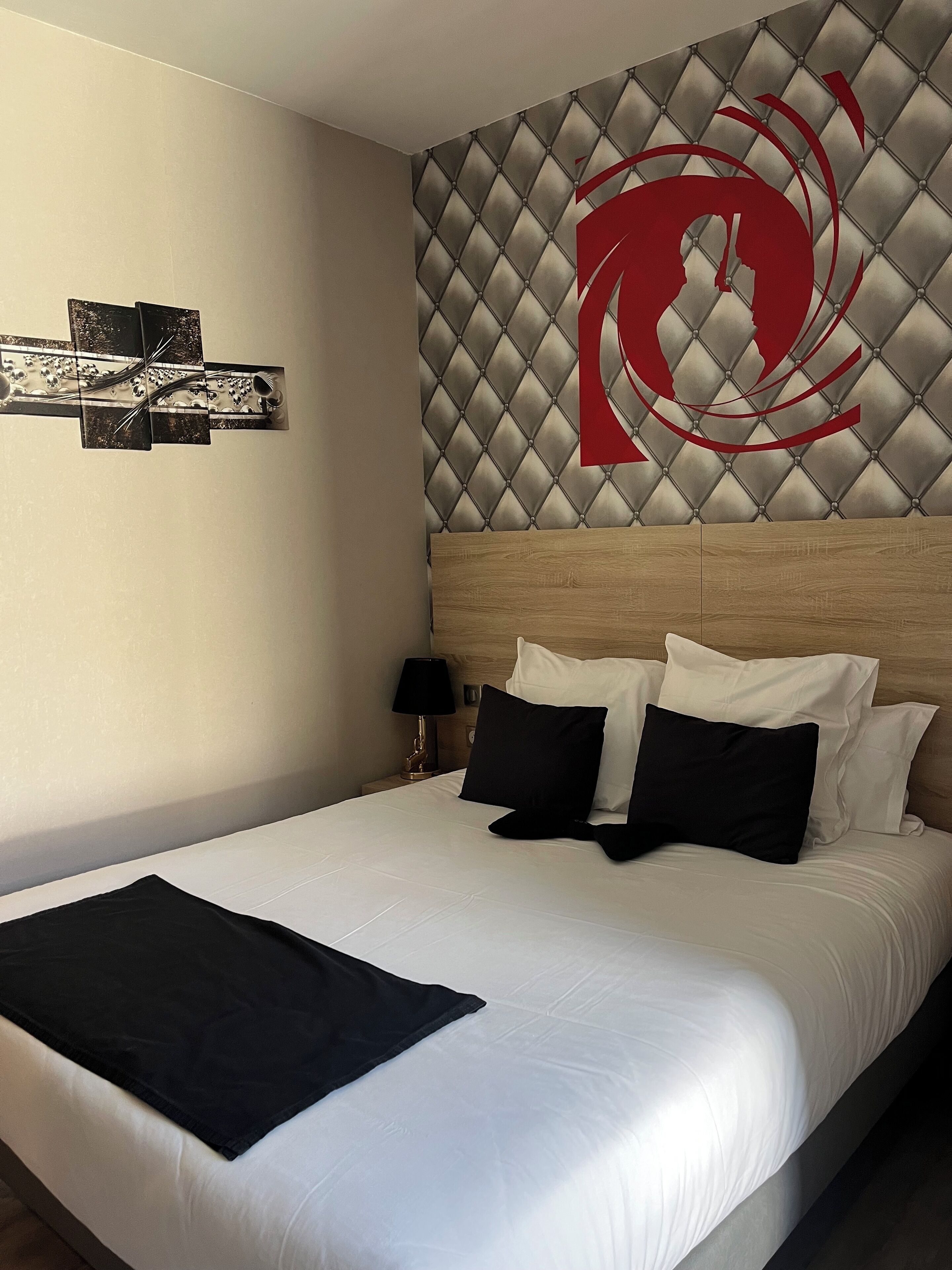 Une chambre d’hôtel avec un grand lit, une tête de lit ornée d’un motif en losanges et une œuvre d’art accrochée au mur.