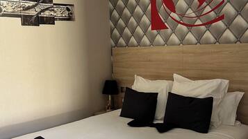A hotel room with a large bed, a headboard with a diamond-patterned design, and a wall-mounted artwork.