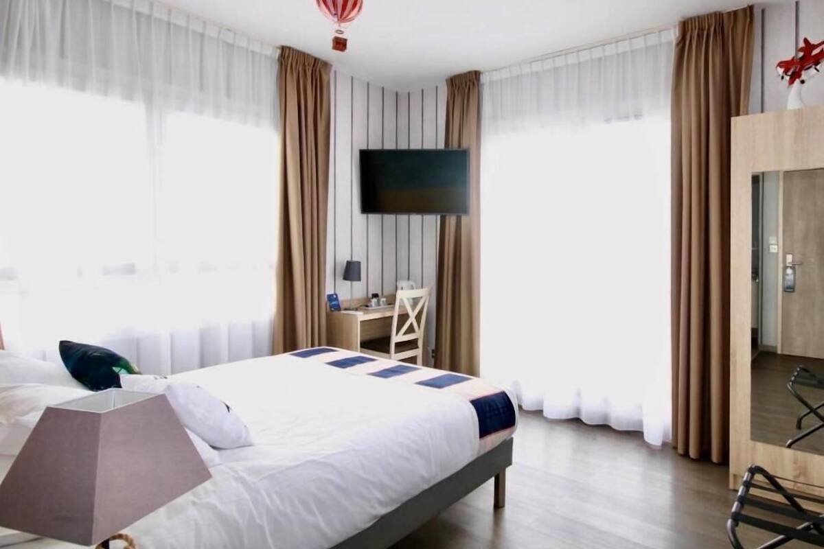 A hotel room with a bed, a desk, a chair, a TV, and a wardrobe.