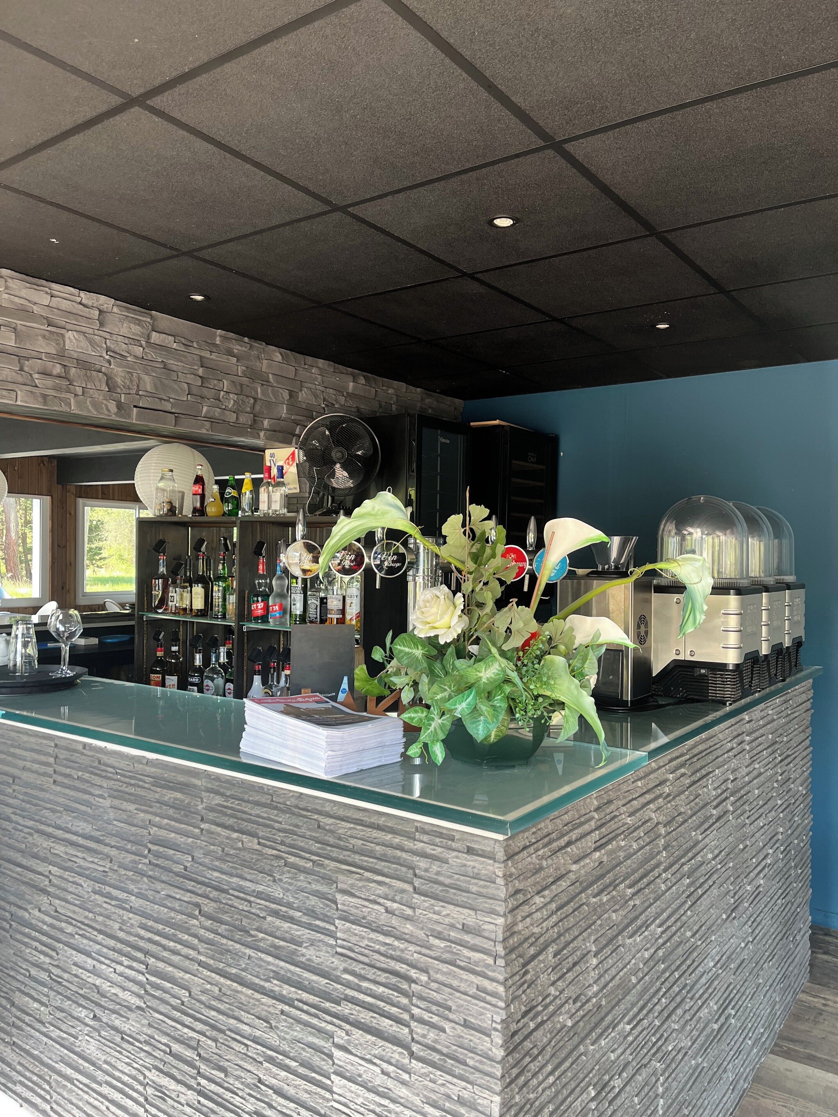 A bar area with a stone wall, shelves with bottles, a fan, and a glass counter with a plant.
