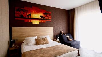 Et hotelværelse med en stor seng, et natbord, en stol og et kunstværk, der viser et savanne landskab.