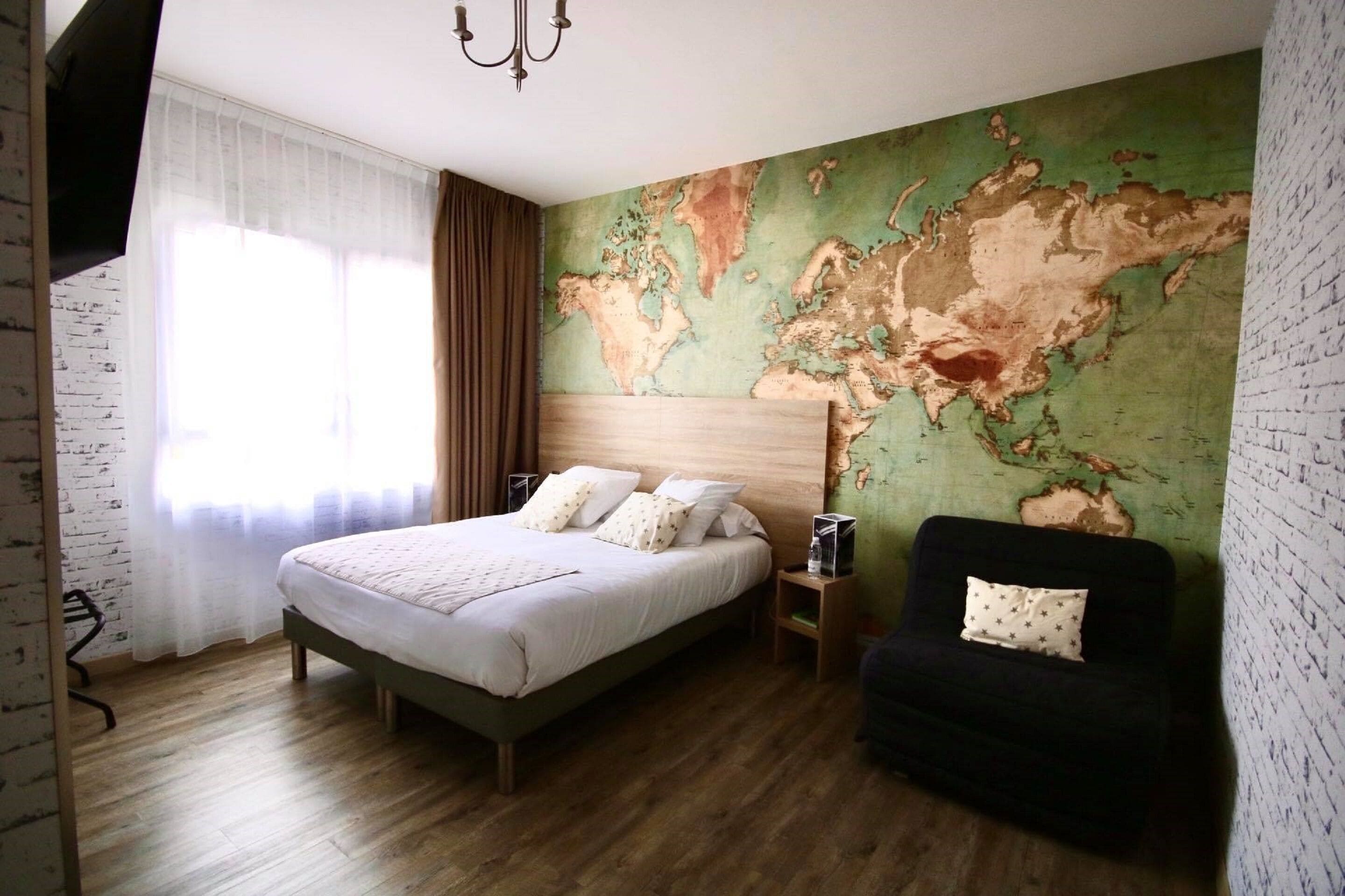 A bedroom with a large bed, a black armchair, a world map on the wall, and a wooden floor.