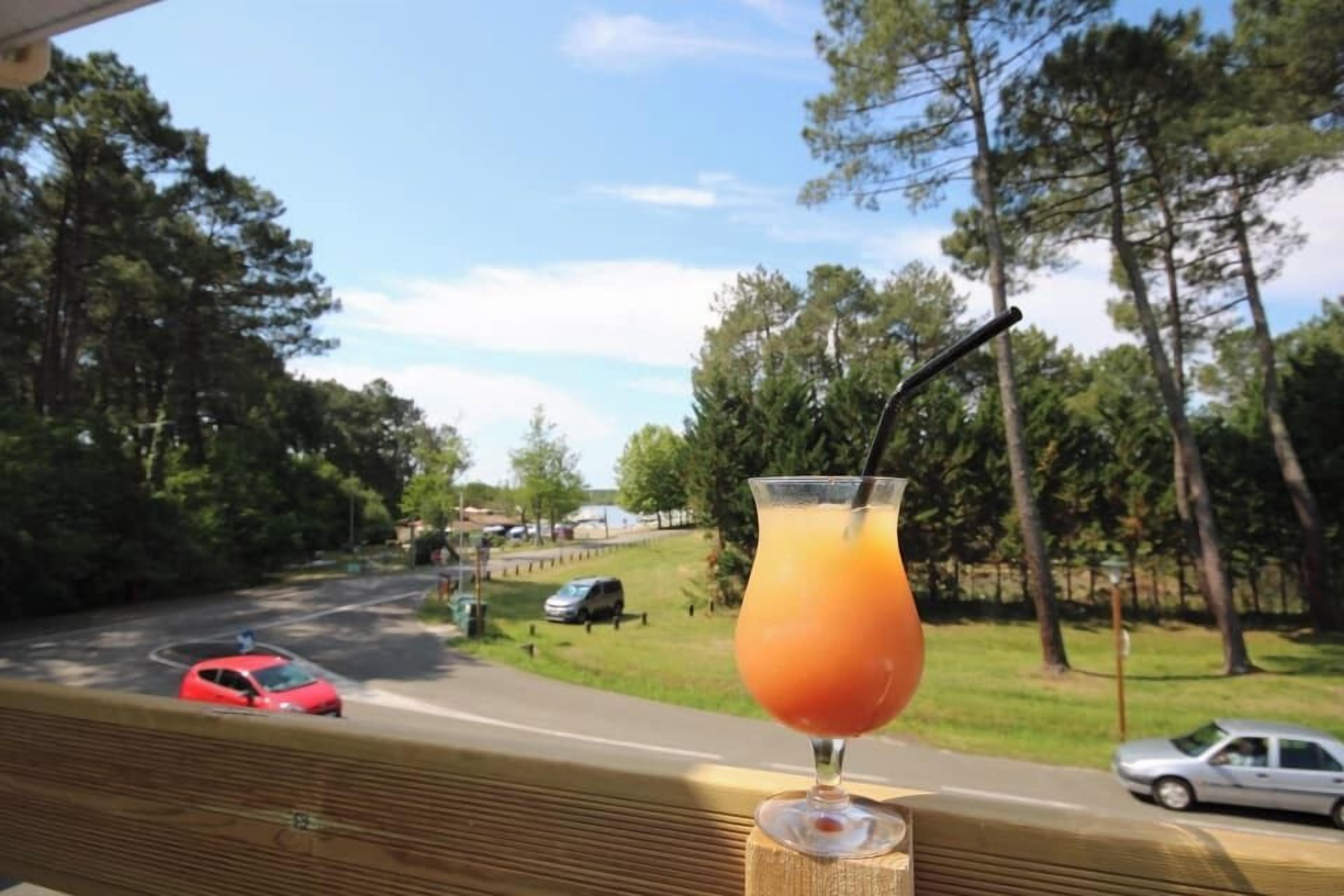 A drink on a table with a view of a road and trees.