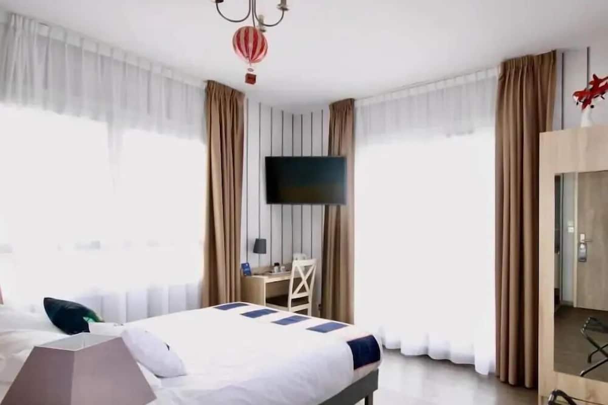 A hotel room with a bed, a desk, a chair, a TV, and curtains.