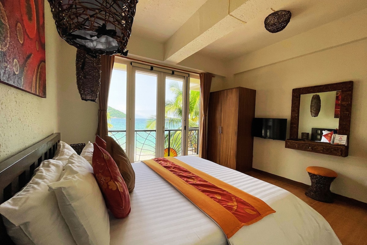 A hotel room with a bed, a window with a view of the ocean, a wardrobe, and a small stool.
