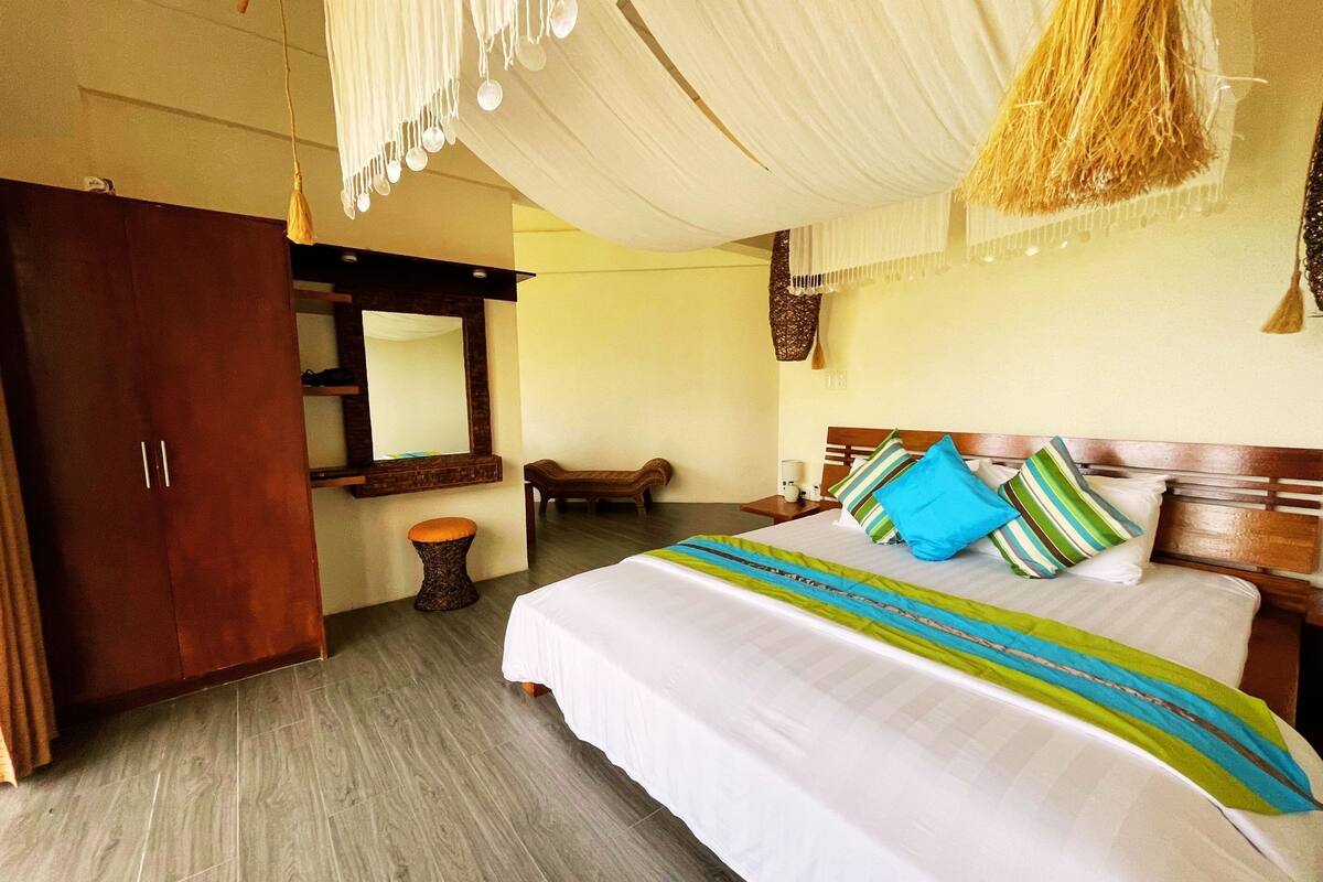 A bedroom with a large bed, wooden wardrobe, and a bench.