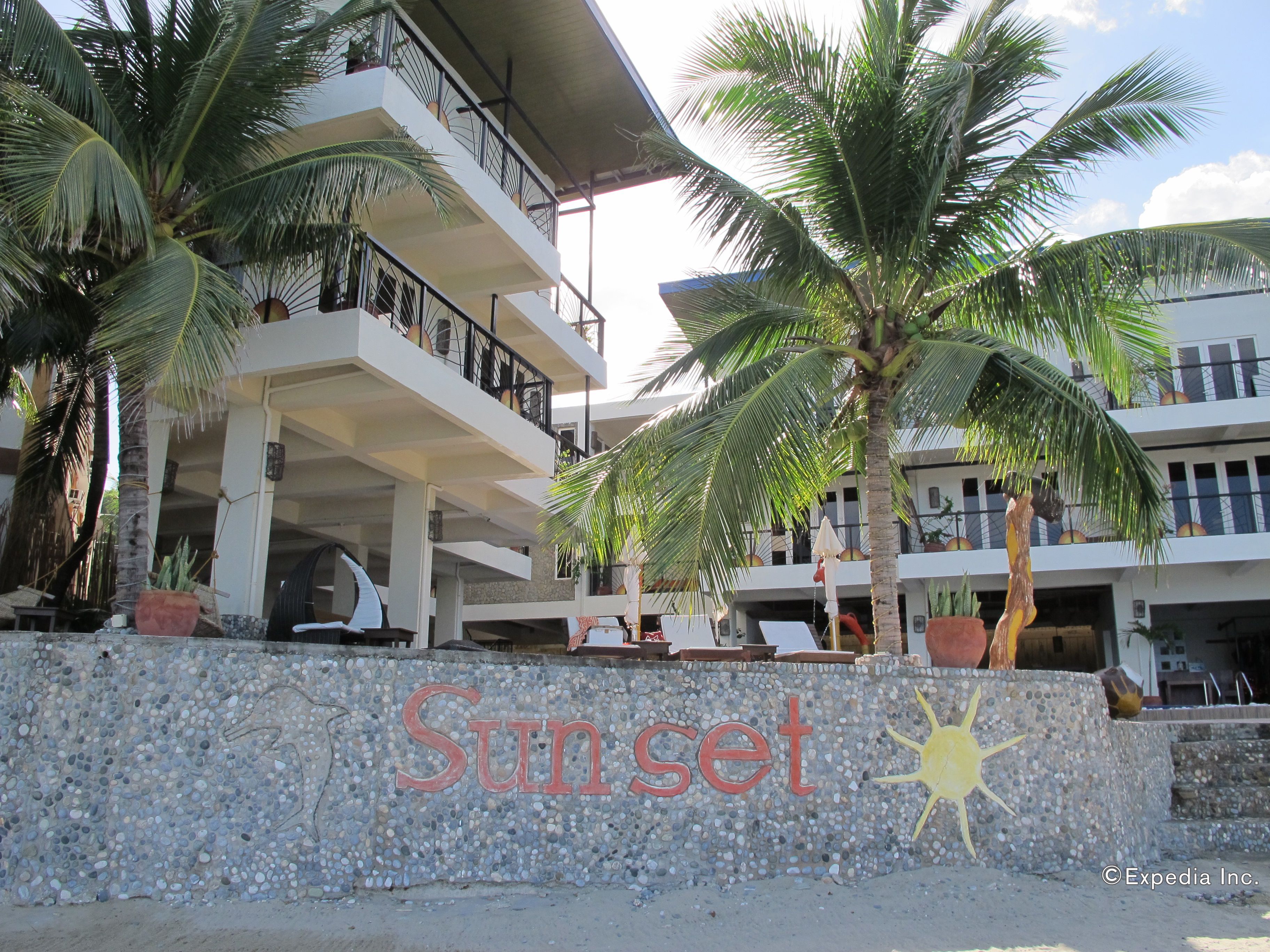 A multi-story building with balconies, palm trees, and a sign reading "Sunset".