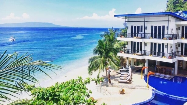 Una propiedad frente a la playa con piscina, un edificio de dos pisos y vista al océano.