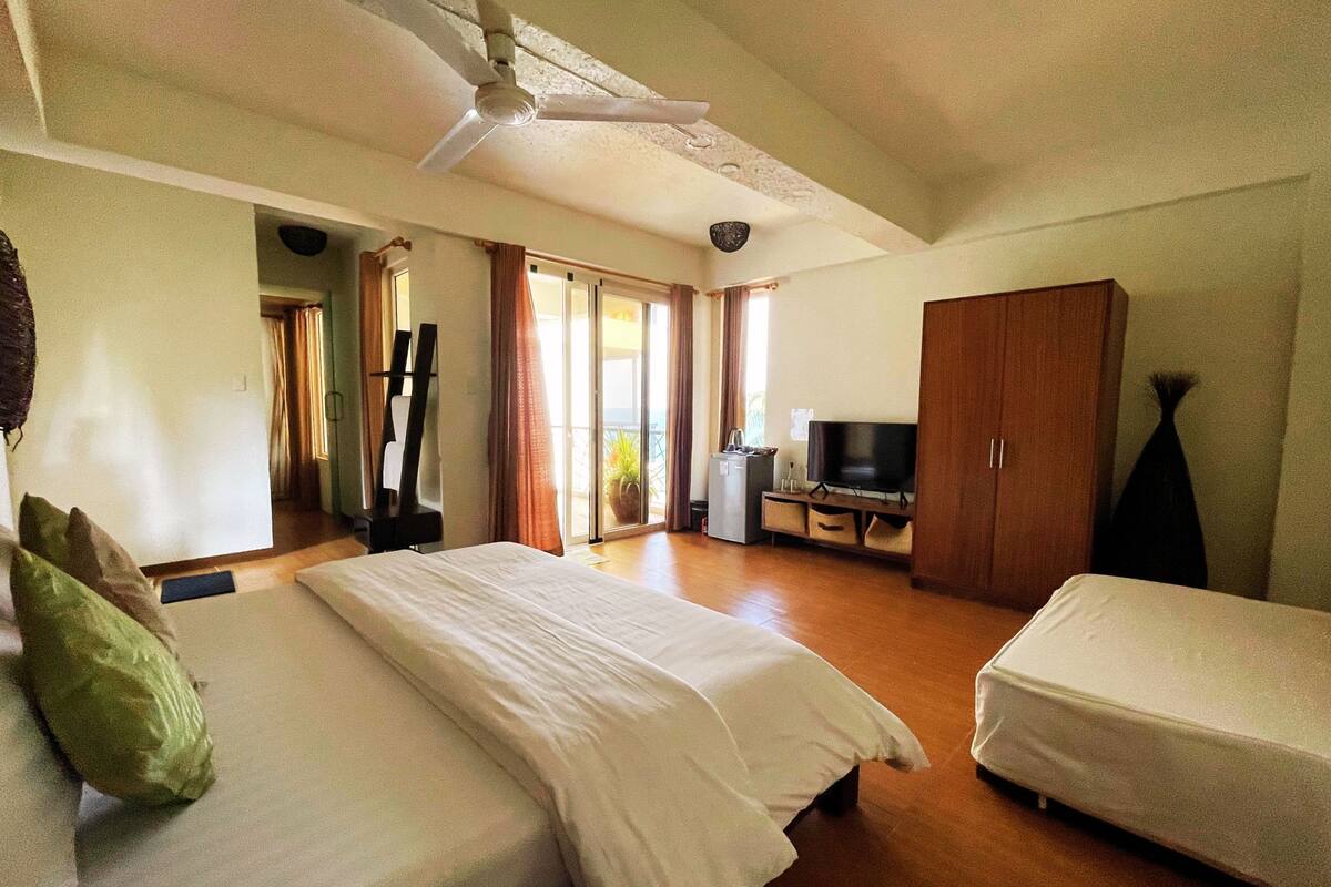 A hotel room with two beds, a television, a wardrobe, and a balcony with curtains.