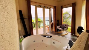 Una habitación con una bañera grande, un balcón con vista al mar y una silla.