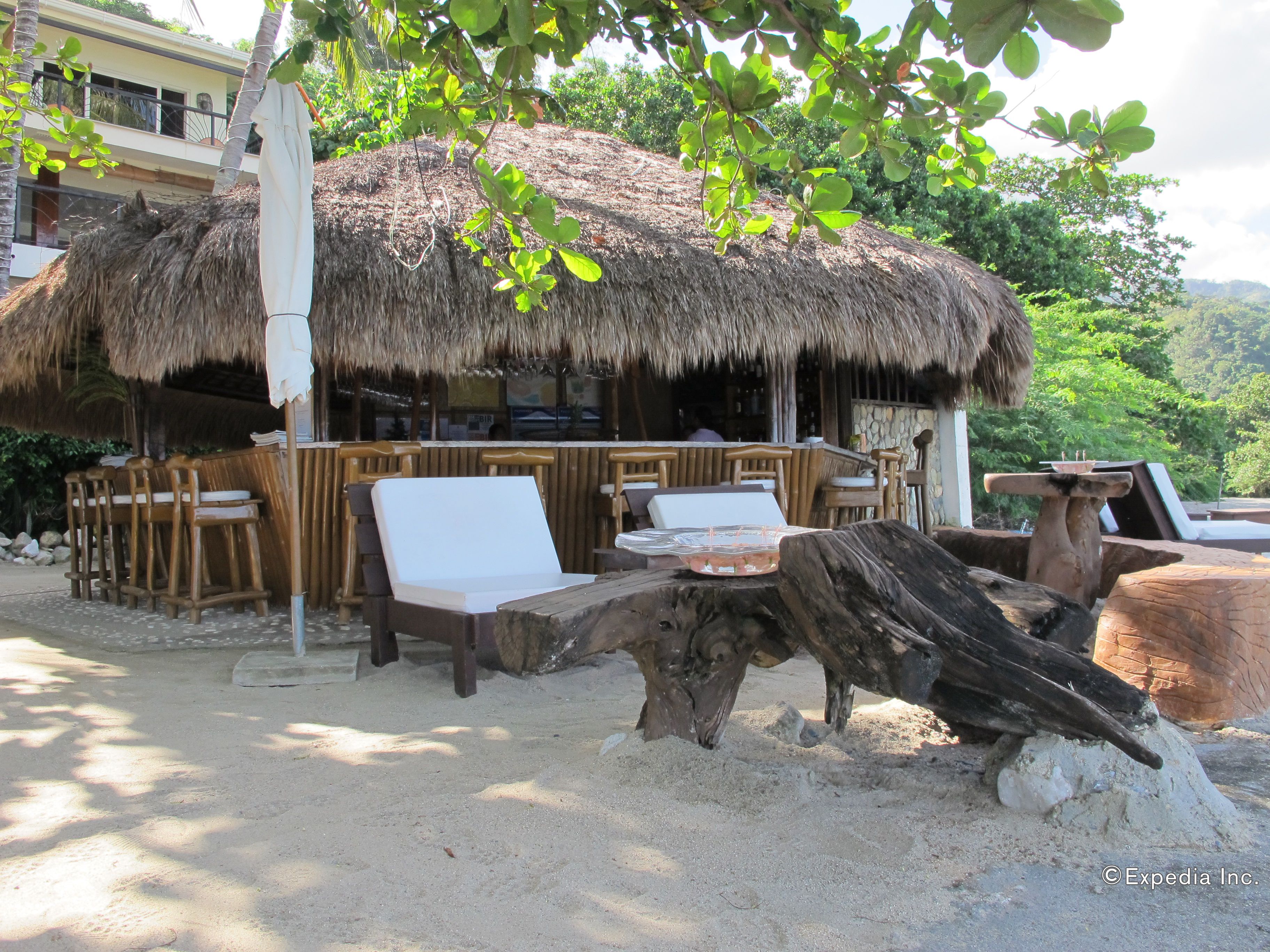 A beachside hut with thatched roof, wooden furniture, and a sandy ground.