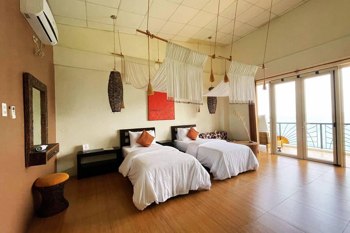 A hotel room with two beds, a large window, and a balcony.