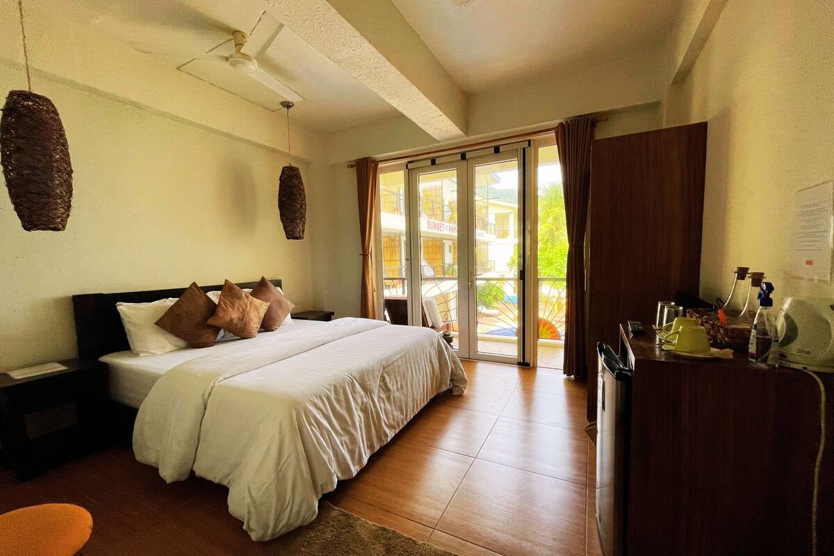 A bedroom with a bed, nightstands, a desk, and a view of the outside.