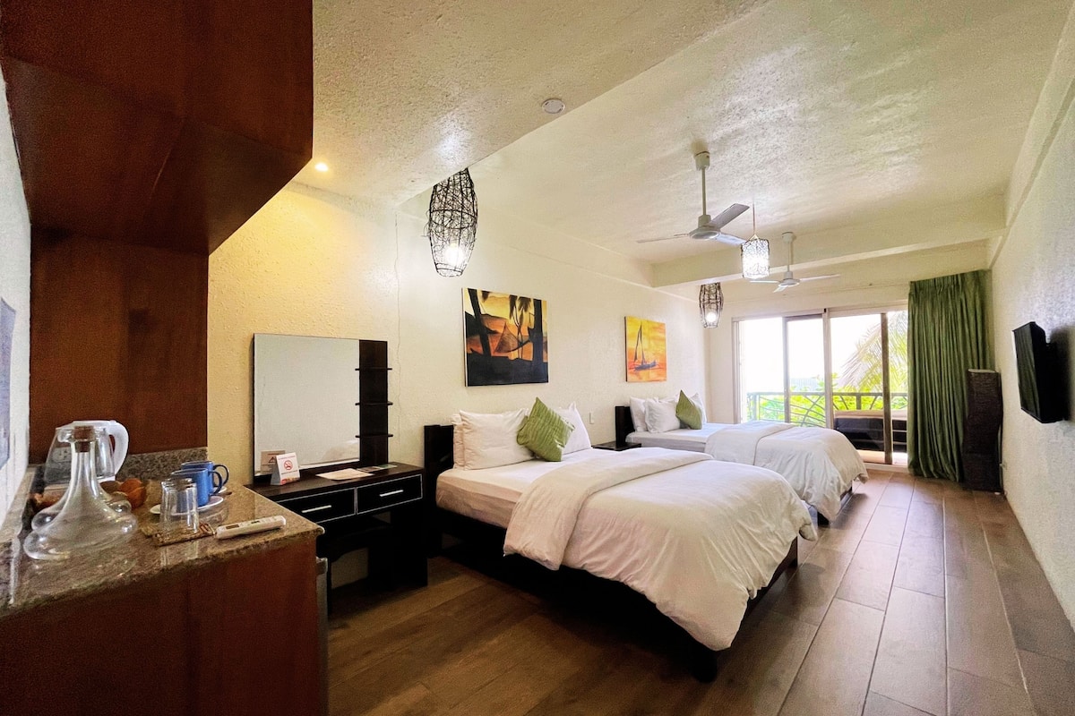 A hotel room with two beds, a large mirror, a desk with a coffee maker, and a balcony with a view.