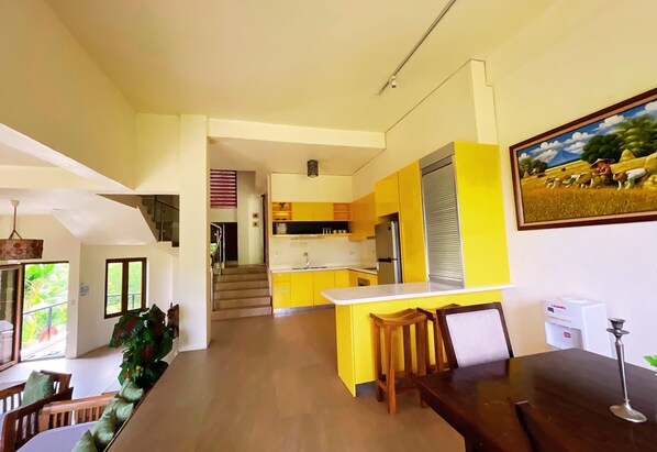 A modern kitchen with yellow cabinets, a white countertop, and a dining area with wooden furniture. - Sunset at Aninuan Beach Resort (Puerto Galera)
