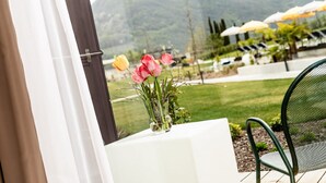 Vista desde una ventana con una mesa y sillas, un florero con flores y un paisaje montañoso al fondo.