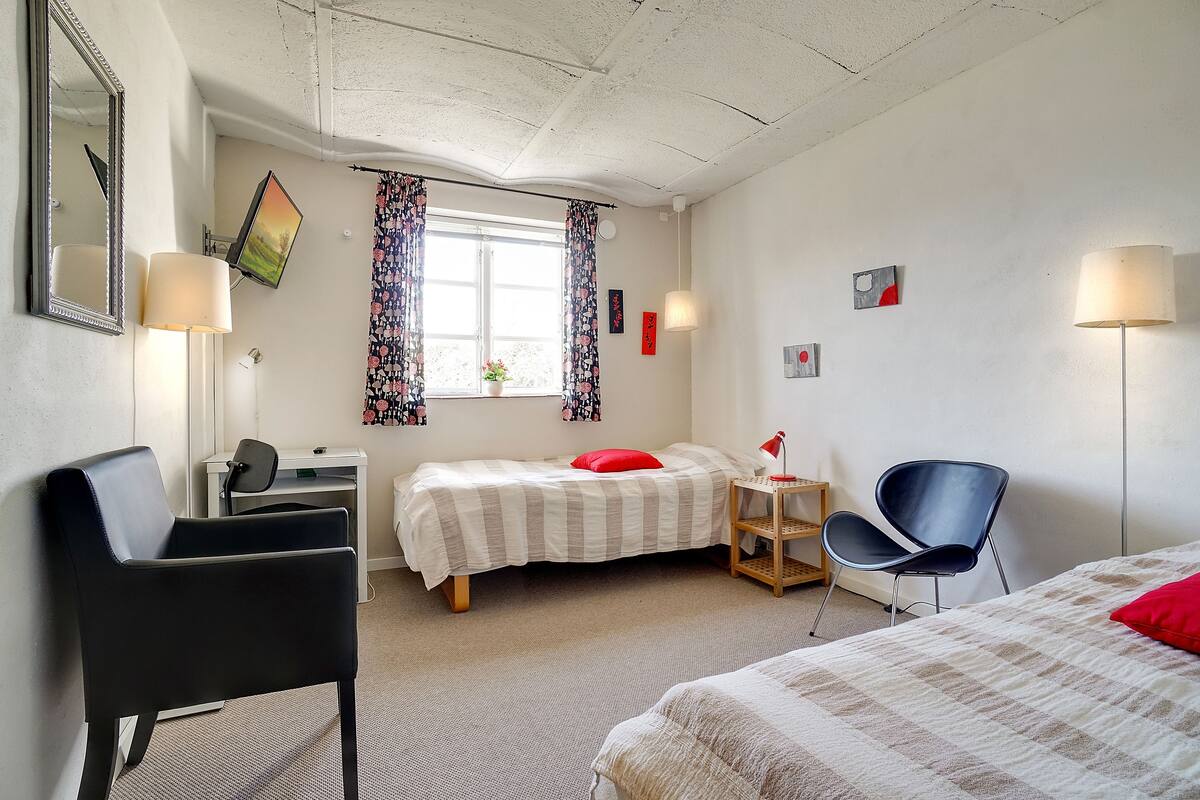 Una habitación de hotel con cama, escritorio, silla, televisor y ventana con cortinas.