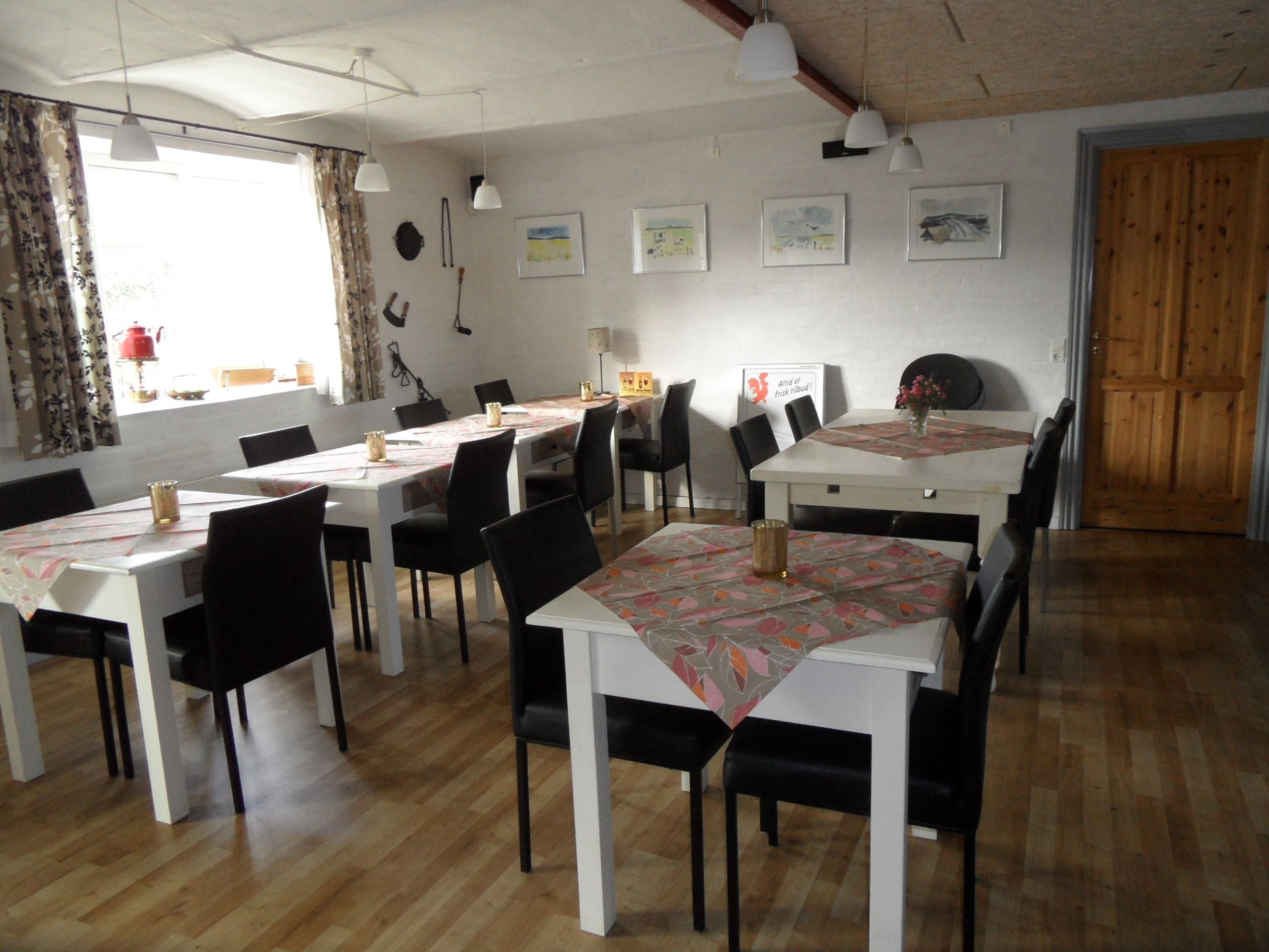 A dining area with multiple tables and chairs, a wooden floor, and a window with curtains.