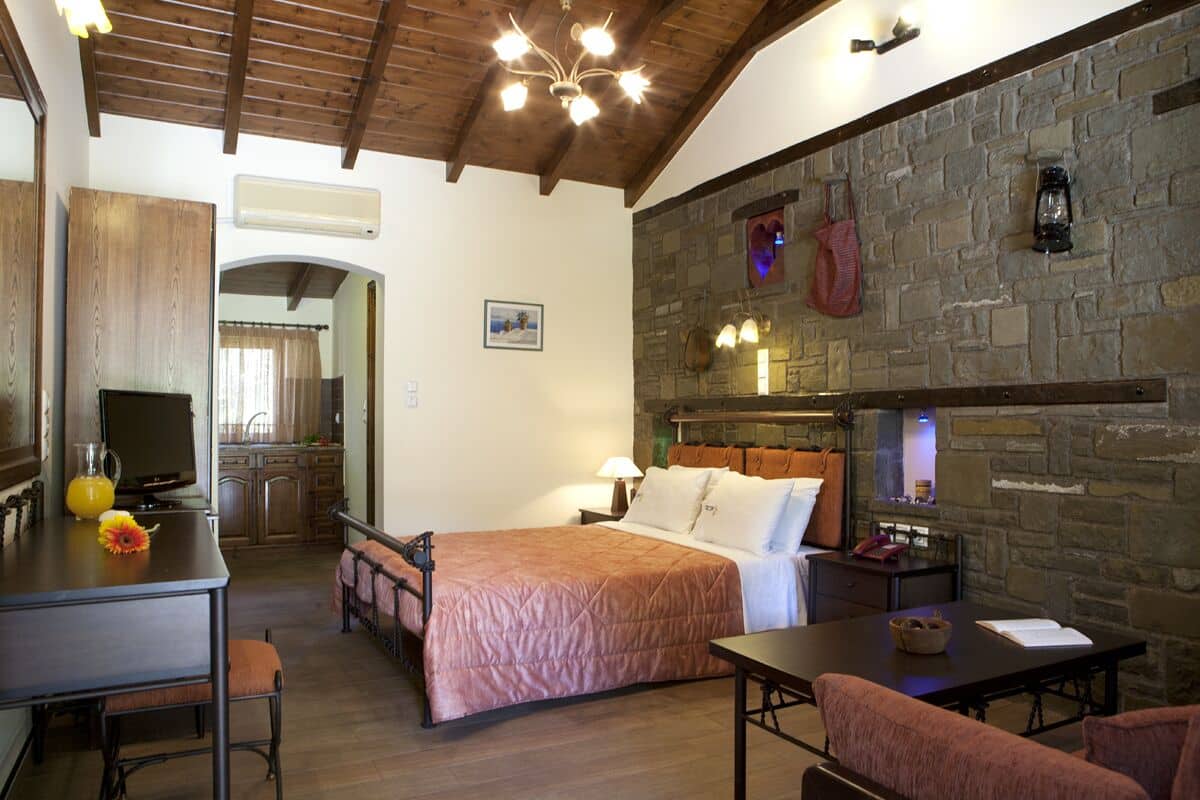 Una habitación acogedora con una cama, una mesa y un televisor. Se aprecia una pared de piedra y un techo de madera.
