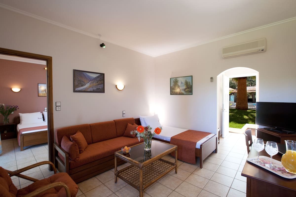 Una sala de estar bien iluminada con un sofá, una mesa de centro y un televisor. Hay cuadros en las paredes y una puerta que da a un espacio al aire libre.