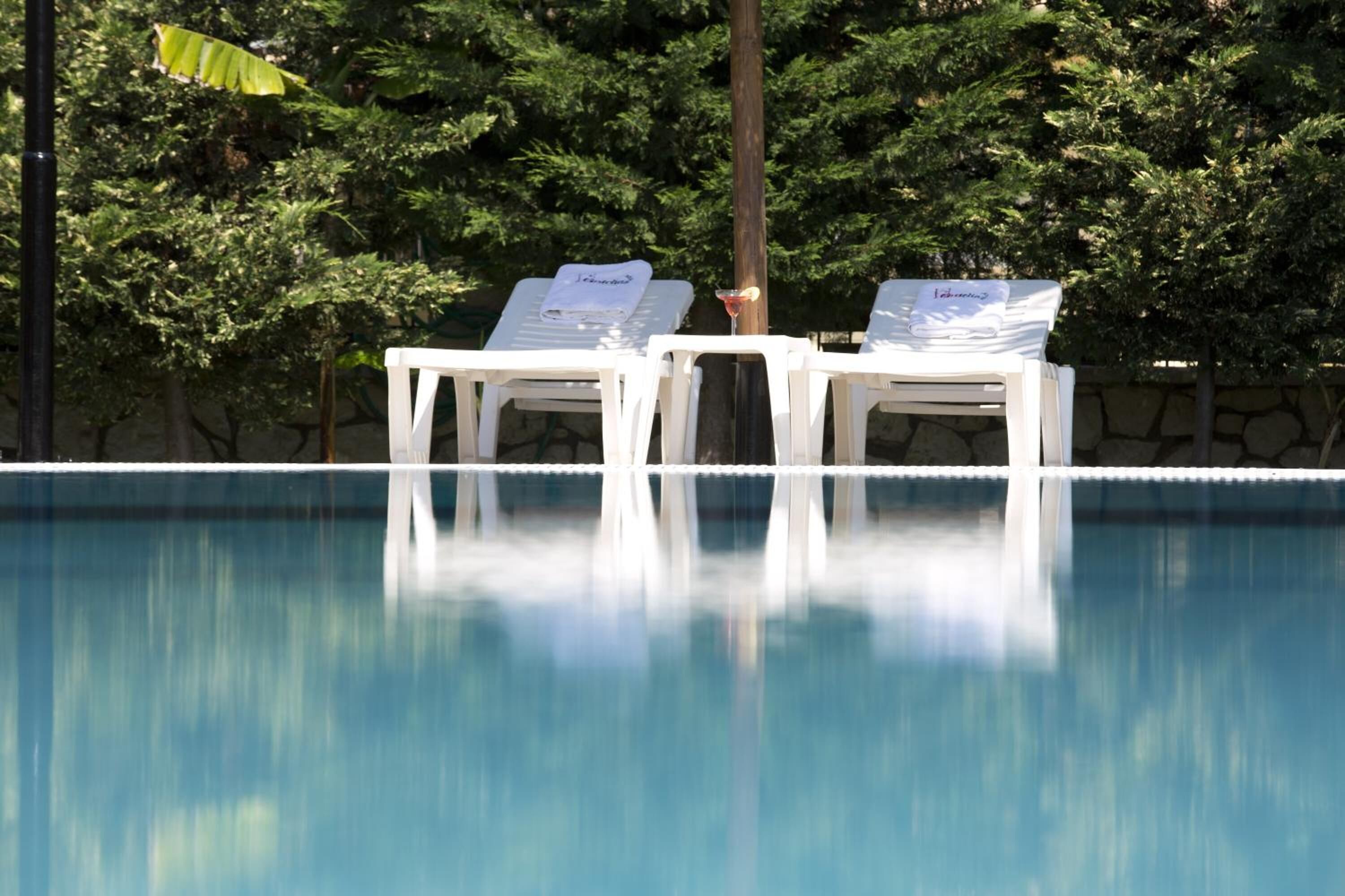 A clear blue pool with two white lounge chairs and a glass of red wine on one of them.