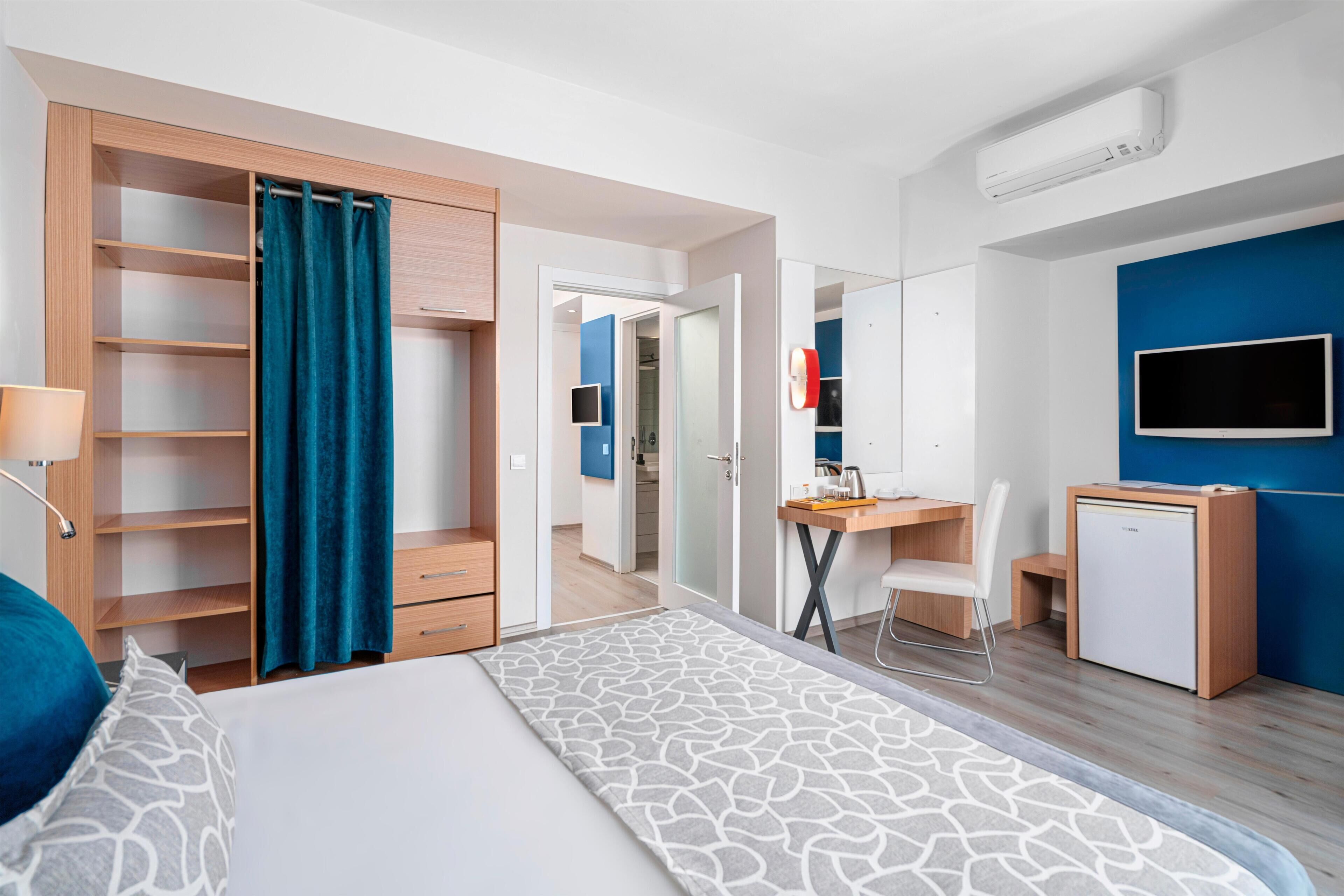 Een moderne hotelkamer met een bed, een bureau, een stoel, een televisie en een kledingkast.